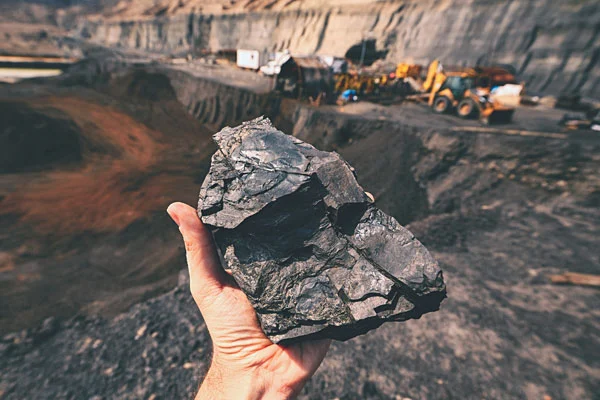 A hand holding a coal with a crane in the background in a coal mine